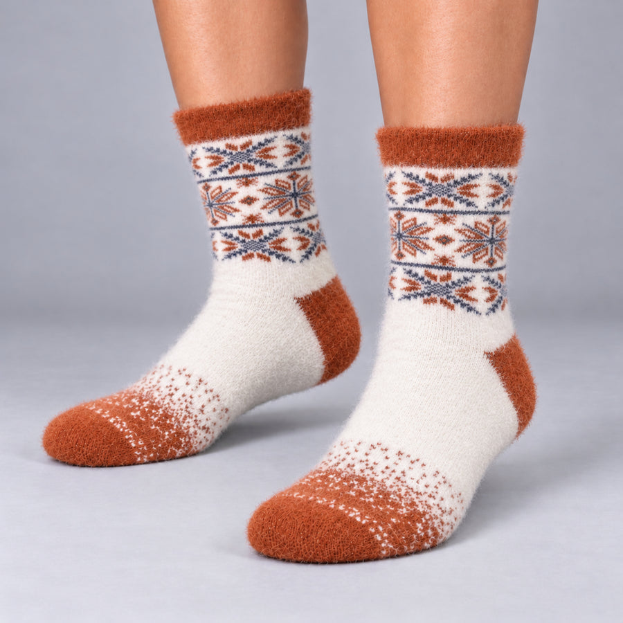 A pair of fuzzy crew socks worn on feet, featuring a cream base with rust orange toes, heels, and cuffs, and a geometric pattern band in rust, navy, and cream.