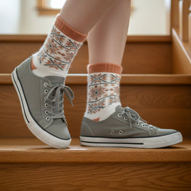 Person wearing gray sneakers and patterned socks standing on wooden stairs.