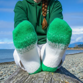 Green and white socks worn by a person sitting on a log by a beach.