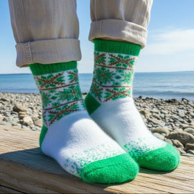Green and white socks worn by a person standing on a log by a beach.