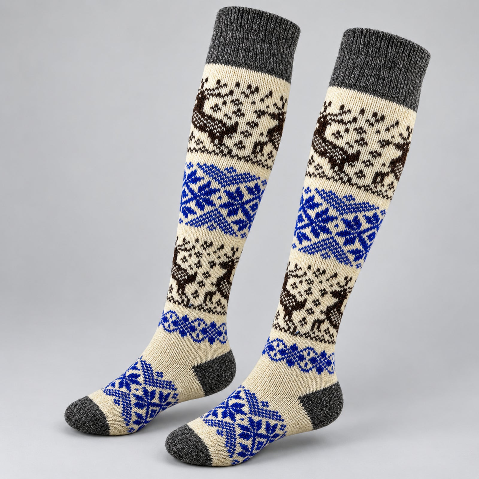 A pair of knee-high knit socks with a traditional Nordic pattern featuring brown reindeer, blue snowflakes, and cream and gray sections, displayed on a light gray background.