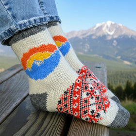 Colorful knitted sock with geometric pattern on a wooden railing with mountains in the background
