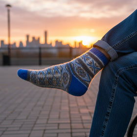 Person wearing patterned socks and blue jeans sitting on a bench with a cityscape and sunset in the background.