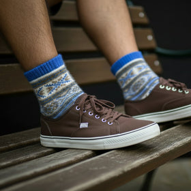Brown sneakers with blue and white patterned socks on a wooden bench.