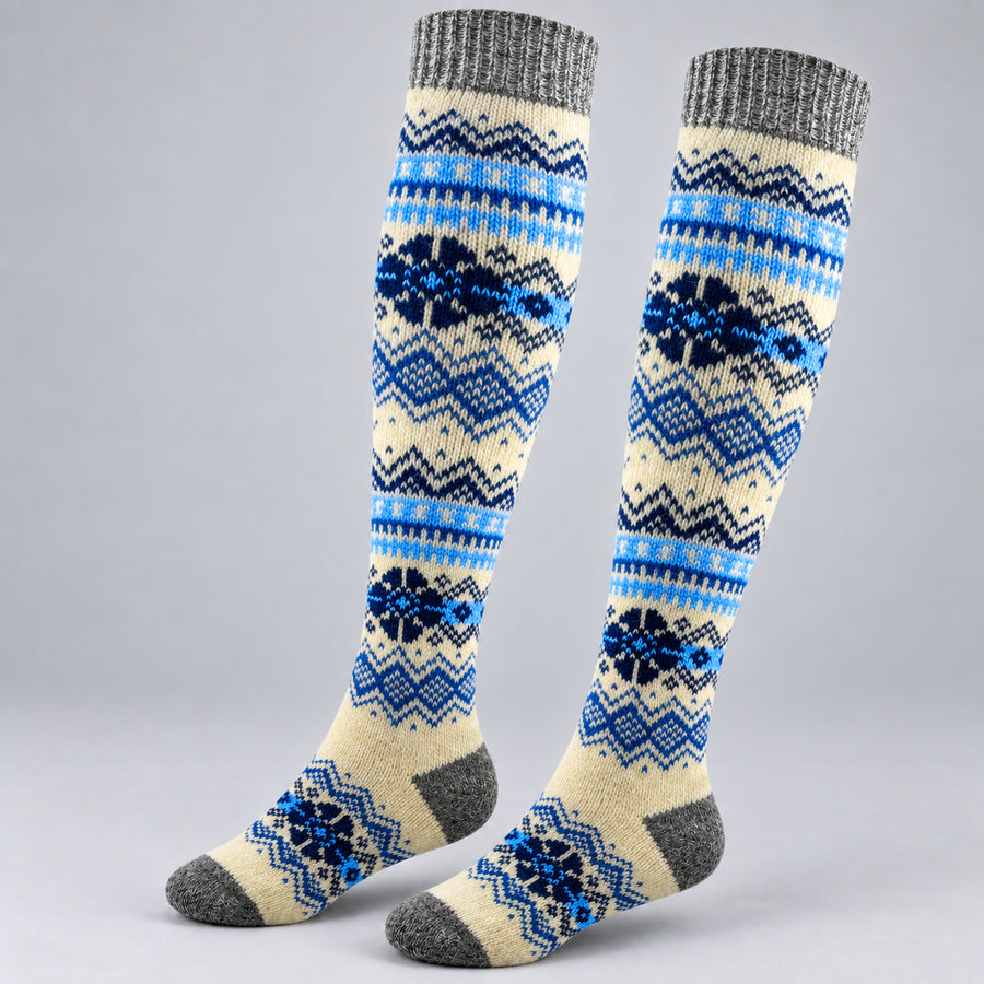 A pair of knee-high knit socks with a Nordic fair isle pattern in blue, navy, and cream, featuring gray ribbed cuffs and toes, displayed against a neutral gray background.