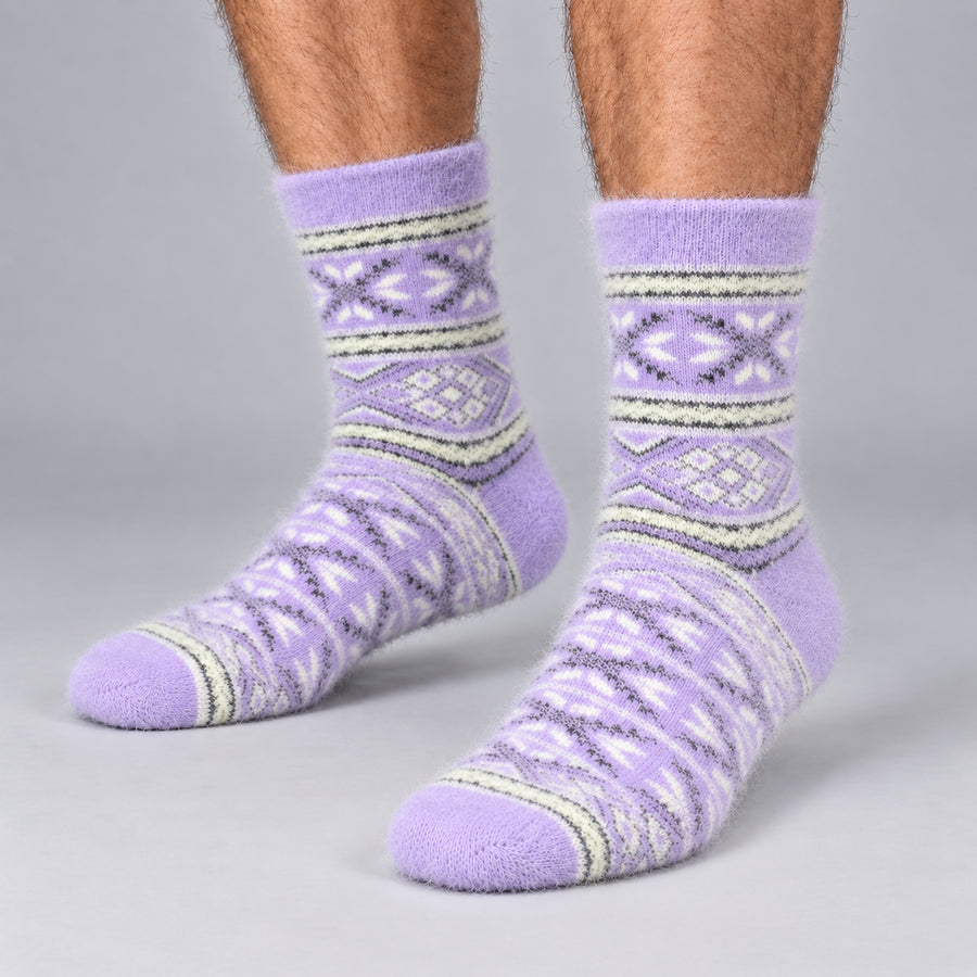 A pair of fuzzy crew socks in lavender purple with a geometric Fair Isle pattern in white and olive green, shown on a person's feet against a neutral gray studio background.