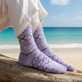 Purple patterned socks on a person's feet sitting on a log at the beach