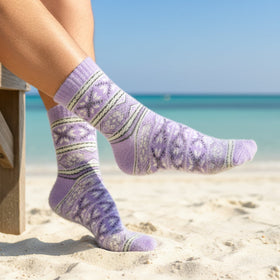 Person wearing purple patterned socks on a beach with clear blue sky and ocean.