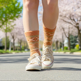 Person wearing patterned socks and white sneakers on a street with cherry blossom trees in the background