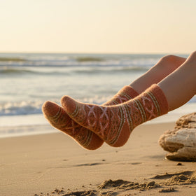 Person sitting on a beach with feet in patterned socks, wearing a white shirt and denim shorts.