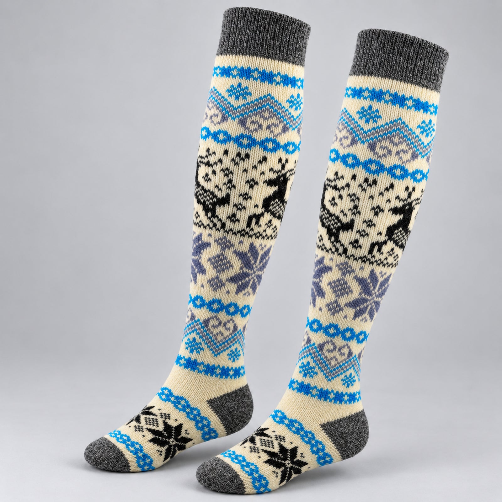 A pair of knee-high knit socks with a Nordic/Fair Isle pattern featuring reindeer, snowflakes, and geometric motifs in blue, gray, black, and cream on a light gray background.