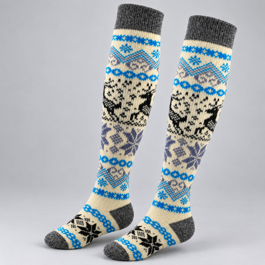 A pair of knee-high knit socks with a Nordic/Fair Isle pattern featuring reindeer, snowflakes, and geometric motifs in blue, gray, black, and cream on a light gray background.