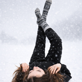 Person lying on their back in the snow wearing dark clothing and patterned socks.