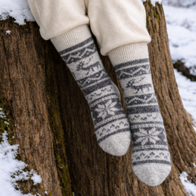 Person wearing patterned socks sitting on a log in a snowy forest
