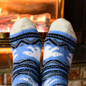Blue and gray patterned socks being worn in front of a fireplace.