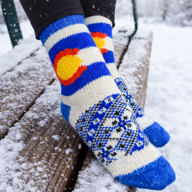 Person wearing colorful knitted socks and mittens in a snowy setting