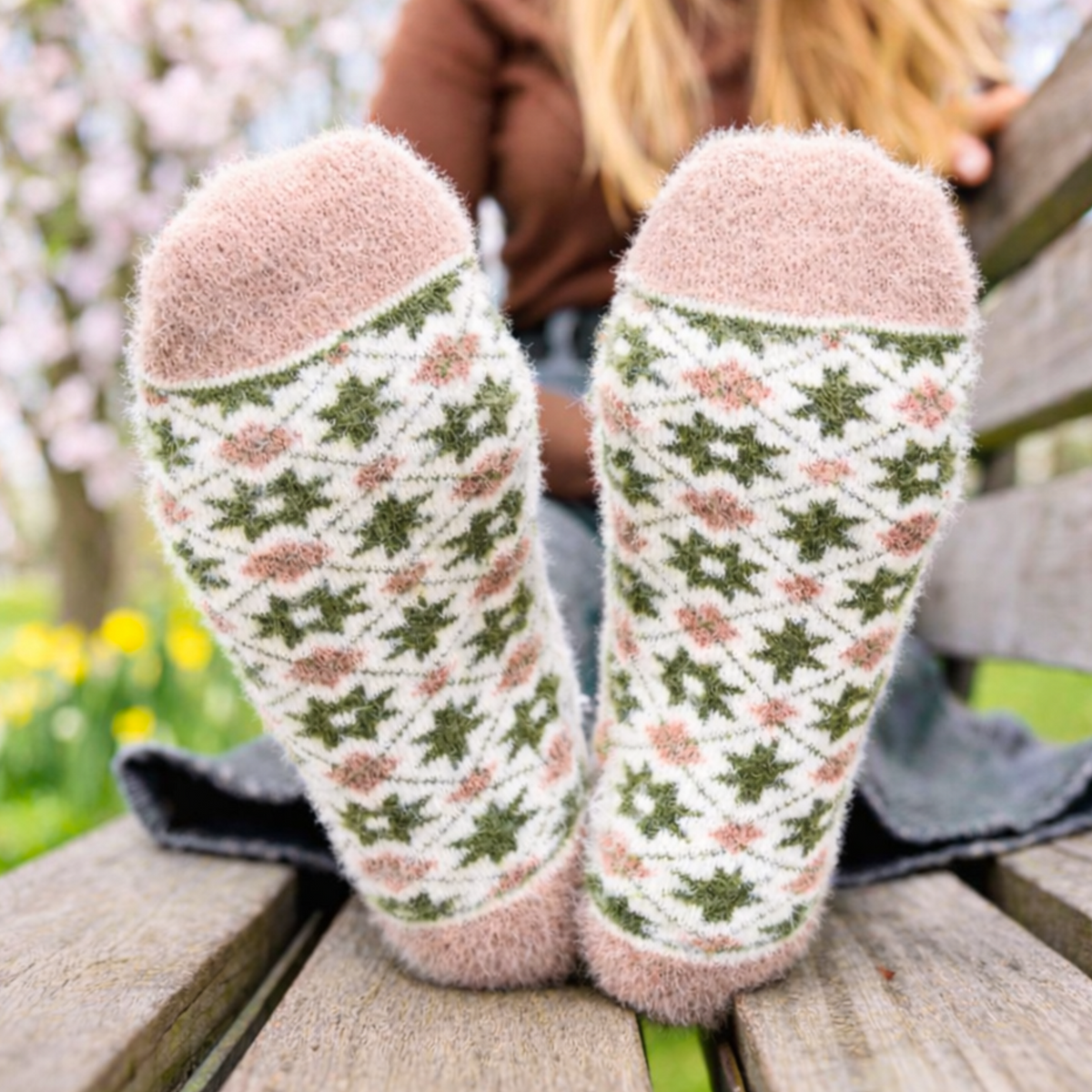 Person wearing patterned socks sitting on a wooden bench with a blurred natural background