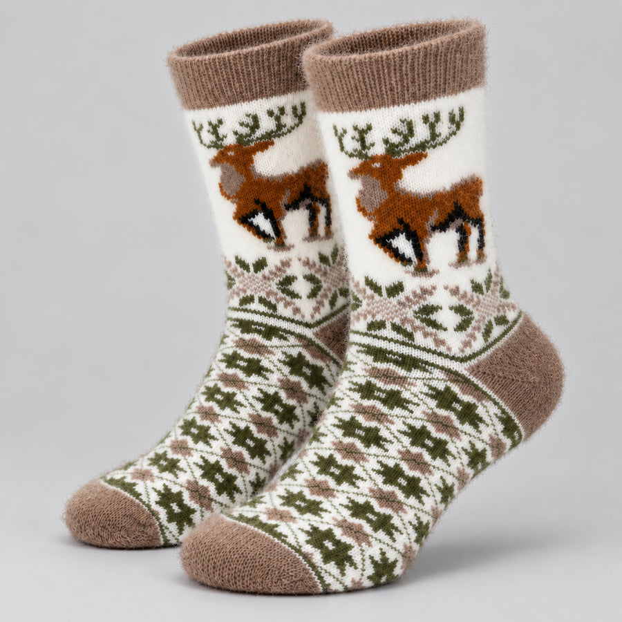 A pair of crew socks with a festive Nordic design, featuring brown reindeer motifs on an off-white background with green and brown geometric patterns, set against a neutral gray studio background.