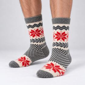 A pair of crew socks with a Nordic fair isle pattern in red, gray, and cream, shown on a person's feet against a light gray studio background.