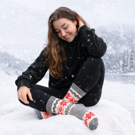 Woman sitting in the snow wearing black leggings and patterned socks.