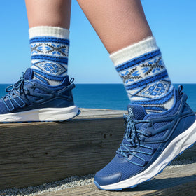 Blue sneakers with blue and gray patterned socks against a blue sky and ocean background