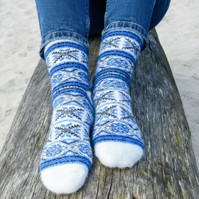 Blue and white patterned socks worn on a wooden bench with a sandy background