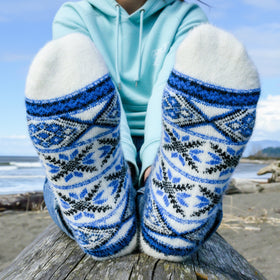 Person wearing blue and white patterned socks sitting on a log by the beach.
