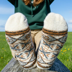 Person wearing patterned socks with a green hoodie and beige pants, sitting on a log in a grassy area.