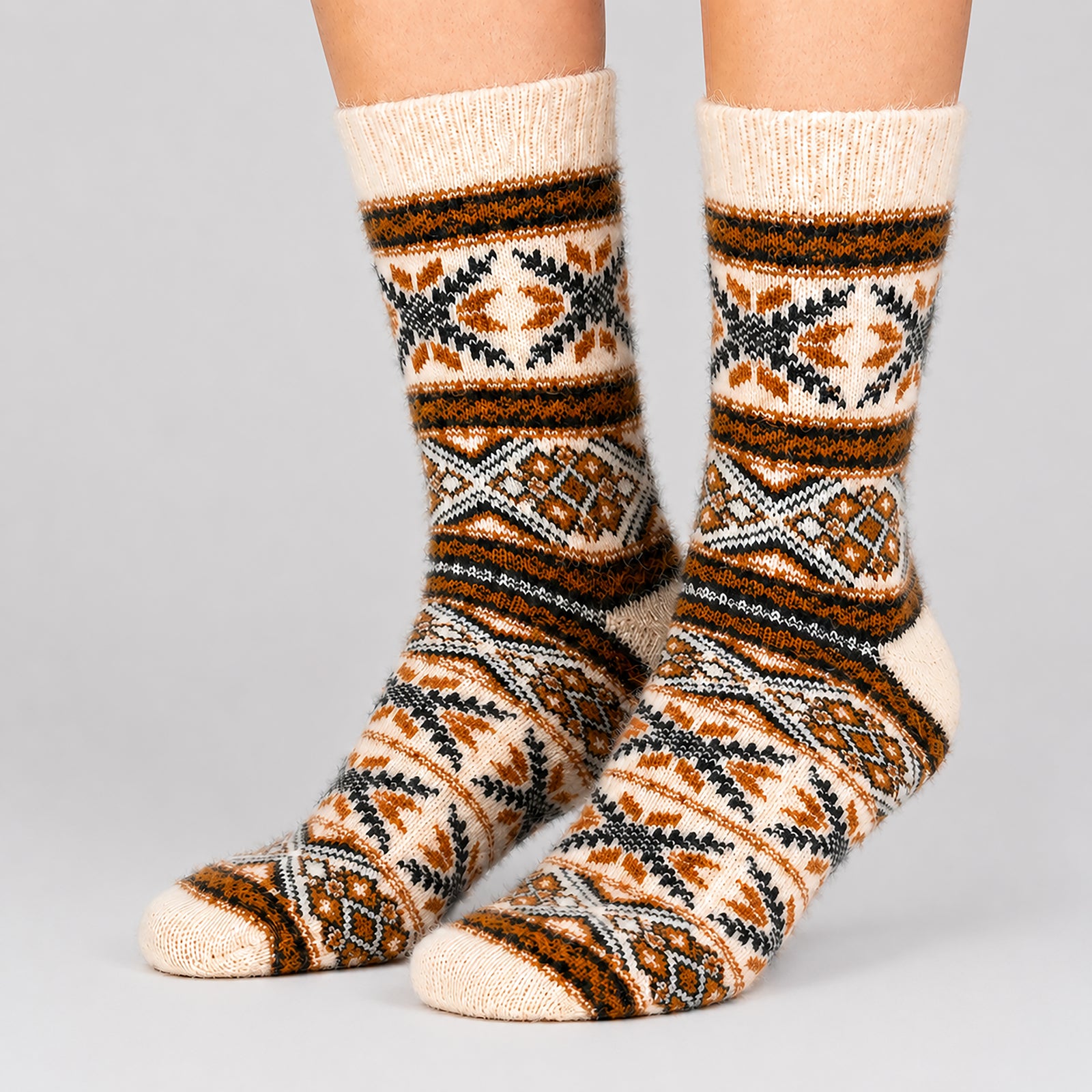 A pair of crew socks with a geometric tribal pattern in cream, brown, black, and gray, shown on a person's feet against a light gray background.