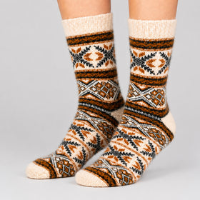 A pair of crew socks with a geometric tribal pattern in cream, brown, black, and gray, shown on a person's feet against a light gray background.