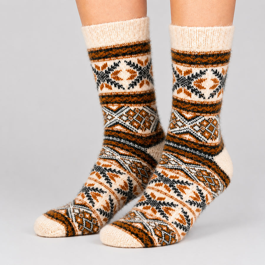 A pair of crew socks with a geometric tribal pattern in cream, brown, black, and gray, shown on a person's feet against a light gray background.