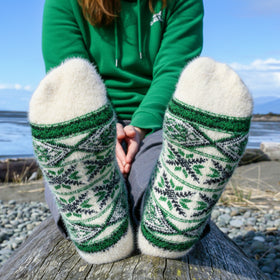 Person wearing green and white patterned socks sitting on a log by a body of water.