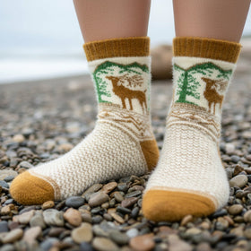 Person wearing patterned socks with deer design on a pebbly beach.
