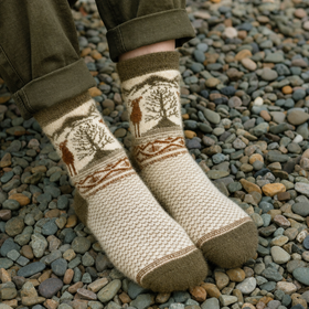 Knitted socks with nature-themed design worn on a pebbly ground