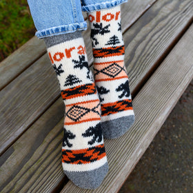 Person wearing patterned socks with 'Color' branding, sitting on a wooden bench.