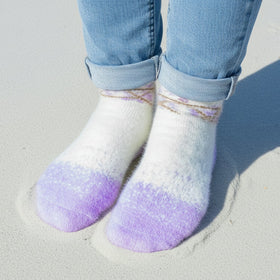 White socks with purple toes and heels worn with light blue jeans on a sandy surface.