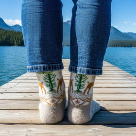 Person wearing patterned socks standing on a wooden dock over a lake with mountains in the background