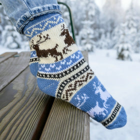 Knitted socks with a winter design on a wooden bench in a snowy landscape