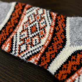 Close-up of a knitted fabric with orange, black, and white pattern on a wooden surface