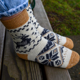 Knitted socks with a pattern worn by a person sitting on a wooden bench.