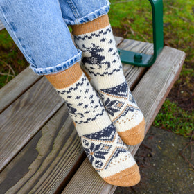 Person wearing patterned socks with blue jeans on a wooden bench outdoors.