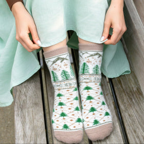 Person wearing patterned socks with trees and flowers on a wooden floor.