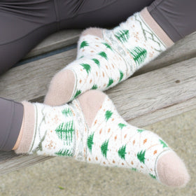 Person wearing white socks with green tree patterns sitting on a wooden bench.