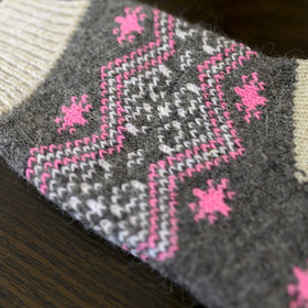 Knitted sock with pink and gray pattern on a wooden surface