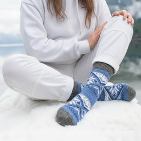 Person wearing blue and white patterned socks sitting on a rock by a lake.