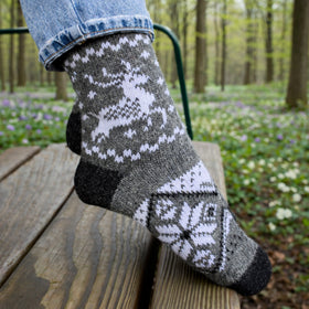 Knitted sock with deer pattern worn by a person in a forest setting