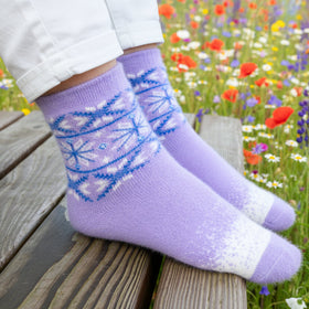 Purple socks with blue floral patterns worn by a person sitting on a wooden bench in a field of flowers.
