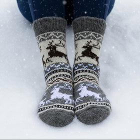 Gray socks with reindeer pattern worn by a person on a white surface